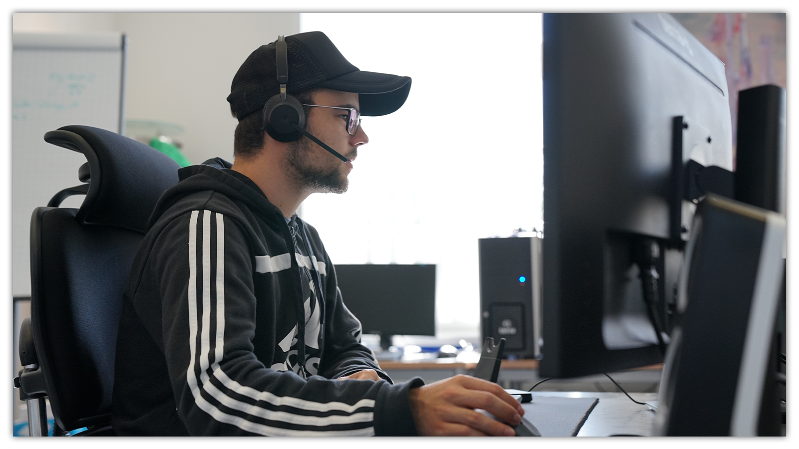 Foto von einem jungen Mann der ein Headset trägt und an einem Computer sitzt